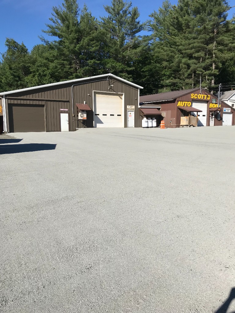 Large finished grey gravel lot in front of industrial metal buildings with roll-up doors under a clear sky.